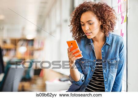 Female digital designer on office desk looking at smartphone View Large Photo Image Stock Photo - Female digital designer on office desk looking at smartphone. Fotosearch