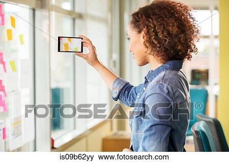 Stock Photo - Female digital designer photographing adhesive notes on office wall. Fotosearch
