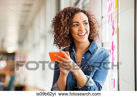 Female digital designer with smartphone looking over her shoulder in office View Large Photo Image Stock Photograph - Female digital designer with smartphone looking over her shoulder in office. Fotosearch