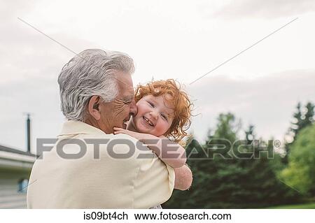 Stock Image - Female toddler with curly red hair in grandfather's arms, portrait. Fotosearch