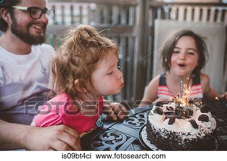 Female toddler with sister and father blowing out sparklers on celebration cake at patio table View Large Photo Image Stock Image - Female toddler with sister and father blowing out sparklers on celebration cake at patio table. Fotosearch