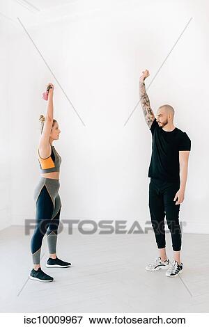 Stock Photo - Fitness instructor teaching woman lifting kettlebell in studio. Fotosearch