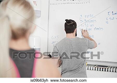 Stock Image - Fitness instructor writing on whiteboard in cross training gym. Fotosearch