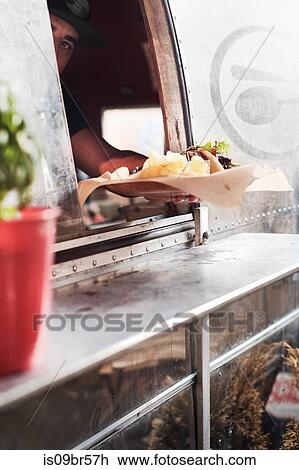 Stock Image - Food being served through window of camper van food truck. Fotosearch