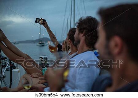Four friends sitting on boat at dusk, drinking wine, taking selfie, British Virgin Islands View Large Photo Image Picture - Four friends sitting on boat at dusk, drinking wine, taking selfie, British Virgin Islands. Fotosearch