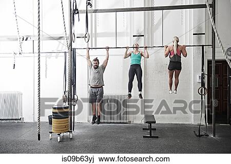 Stock Image - Friends doing chin-up in cross training gym. Fotosearch