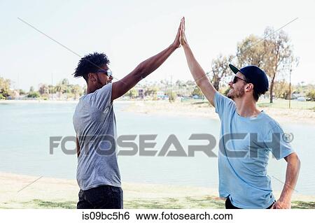 Stock Photograph - Friends doing high five by lake, Long Beach, California, US. Fotosearch