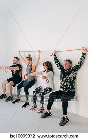 Stock Image - Friends doing squat against wall with resistance band. Fotosearch