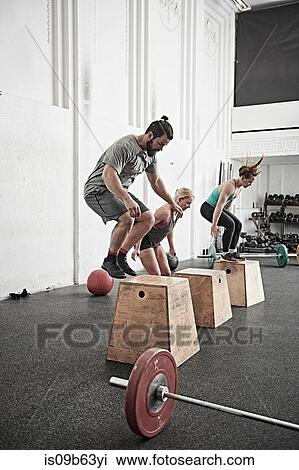 Stock Image - Friends jumping onto fitness box in cross training gym. Fotosearch