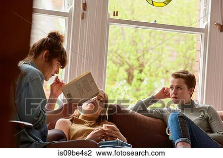 Stock Image - Friends reading book on sofa. Fotosearch