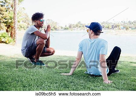 Stock Photography - Friends relaxing on grass by lake, Long Beach, California, US. Fotosearch