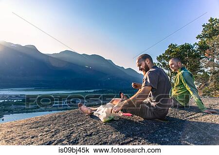 Stock Image - Friends relaxing on mountain ledge overlooking lake, Squamish, Canada. Fotosearch