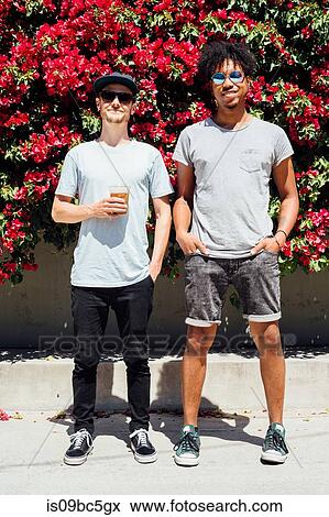 Stock Photo - Friends standing next to each other beside red bougainvilleas. Fotosearch
