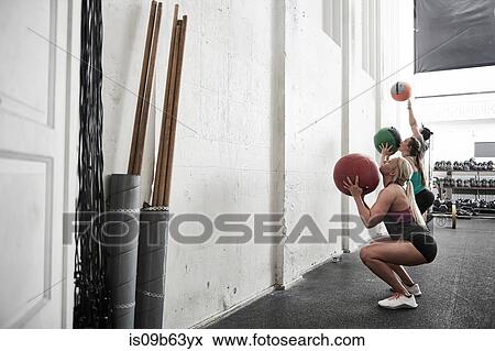 Friends throwing fitness ball against wall in cross training gym View Large Photo Image Stock Photo - Friends throwing fitness ball against wall in cross training gym. Fotosearch