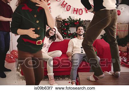 Stock Photo - Friends watching young man dancing on table at christmas party. Fotosearch