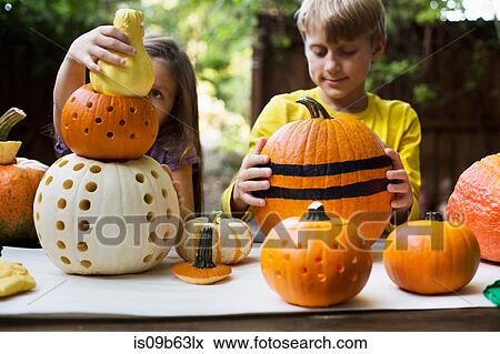 Girl and brother stacking carved pumpkins on garden table View Large Photo Image Stock Photo - Girl and brother stacking carved pumpkins on garden table. Fotosearch