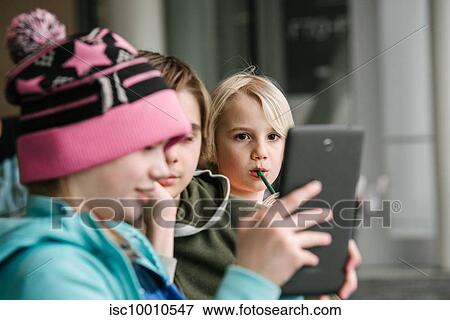 Girl and brothers looking at digital tablet in airport, head and shoulders View Large Photo Image Stock Photo - Girl and brothers looking at digital tablet in airport, head and shoulders. Fotosearch