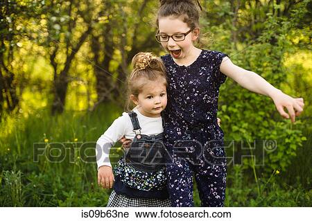Stock Image - Girl and little sister playing in field with trees. Fotosearch
