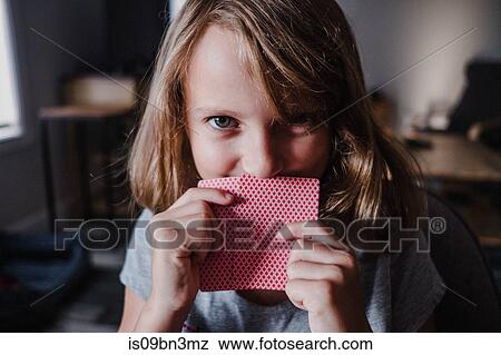 Girl hiding behind playing cards in living room, portrait View Large Photo Image Stock Photo - Girl hiding behind playing cards in living room, portrait. Fotosearch