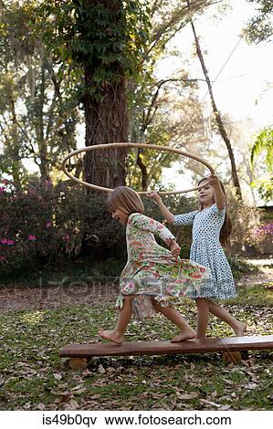 Stock Photo - Girl holding plastic hoop above her sister's head. Fotosearch