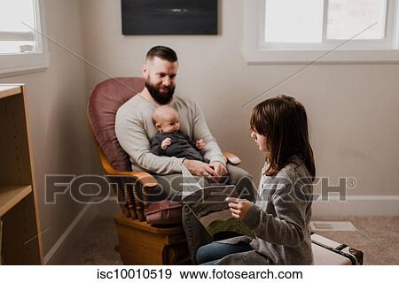 Girl in living room reading book next to father and baby brother on armchair View Large Photo Image Stock Photo - Girl in living room reading book next to father and baby brother on armchair. Fotosearch