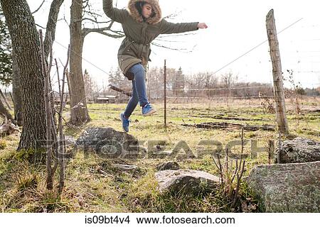 Girl jumping from rock to rock in field View Large Photo Image Picture - Girl jumping from rock to rock in field. Fotosearch