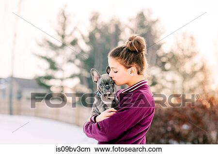 Picture - Girl kissing french bulldog puppy outdoors. Fotosearch