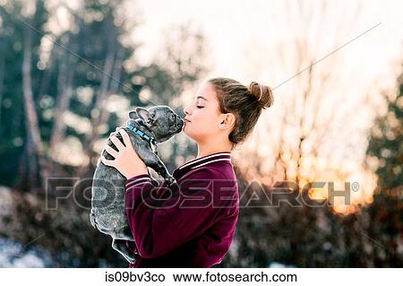 Picture - Girl kissing french bulldog puppy outdoors. Fotosearch