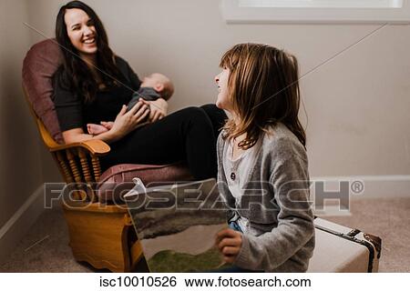 Girl laughing with mother while she cradles baby brother in living room armchair View Large Photo Image Stock Photograph - Girl laughing with mother while she cradles baby brother in living room armchair. Fotosearch