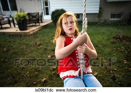 Stock Image - Girl swinging on rope in garden. Fotosearch