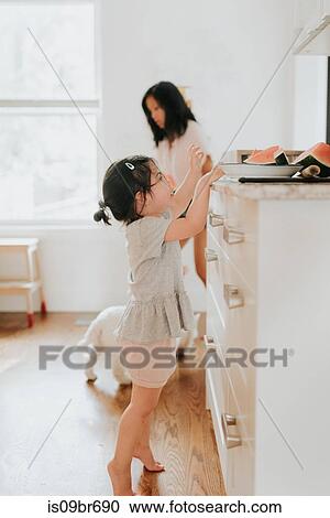 Girl tiptoeing for watermelon in kitchen, mother in background View Large Photo Image Stock Image - Girl tiptoeing for watermelon in kitchen, mother in background. Fotosearch