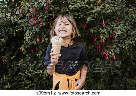 Stock Photo - Girl with ice cream cone in front of hedge. Fotosearch