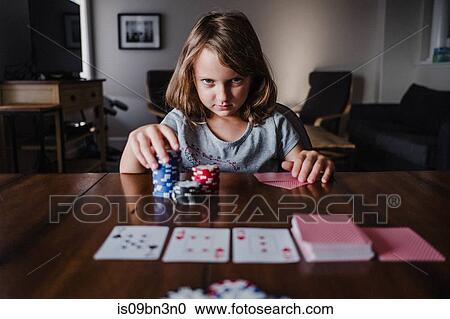 Stock Image - Girl with stack of gambling chips playing cards at table, portrait. Fotosearch
