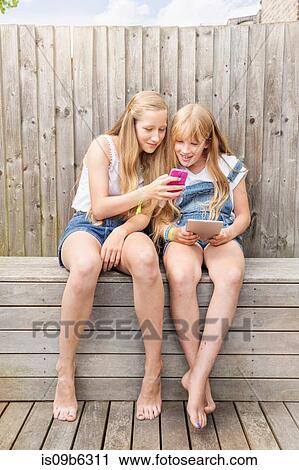 Girls sitting in garden using digital tablet and smartphone smiling View Large Photo Image Stock Image - Girls sitting in garden using digital tablet and smartphone smiling. Fotosearch