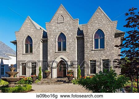 Stock Image - Gothic style house in grey stone with arched windows, facade. Fotosearch