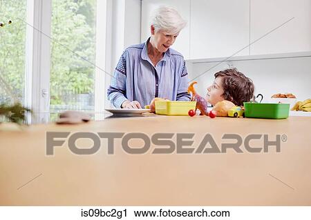 Stock Image - Grandmother and grandson preparing food in kitchen. Fotosearch