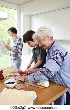Stock Photo - Grandmother and grandson preparing food in kitchen, mother in background. Fotosearch