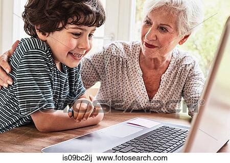 Grandmother and grandson sitting at table, using laptop View Large Photo Image Stock Image - Grandmother and grandson sitting at table, using laptop. Fotosearch