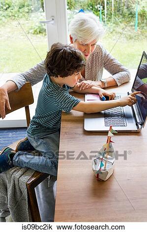 Stock Image - Grandmother and grandson sitting at table, using laptop. Fotosearch