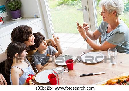 Grandmother sitting at kitchen, photographing grown daughter and grandchildren, using smartphone View Large Photo Image Stock Photo - Grandmother sitting at kitchen, photographing grown daughter and grandchildren, using smartphone. Fotosearch