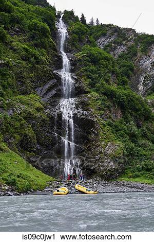 Group of adventure tourists looking at mountain waterfall on river bank, Valdez, Alaska, USA View Large Photo Image Stock Image - Group of adventure tourists looking at mountain waterfall on river bank, Valdez, Alaska, USA. Fotosearch