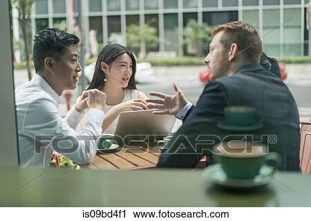 Stock Image - Group of businesspeople, having meeting at cafe, using laptop, outdoors. Fotosearch