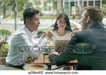 Stock Image - Group of businesspeople, having meeting at cafe, using laptop, outdoors. Fotosearch