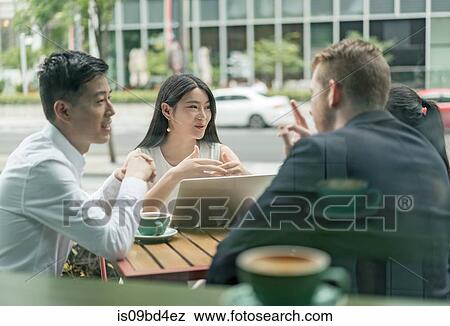 Stock Photo - Group of businesspeople, having meeting at cafe, using laptop, outdoors. Fotosearch