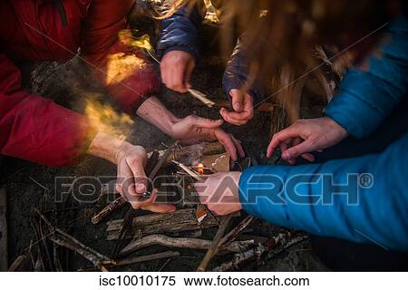 Stock Photography - Group of friends lighting a campfire at dusk, cropped, Tofino, Vancouver Island, Canada. Fotosearch