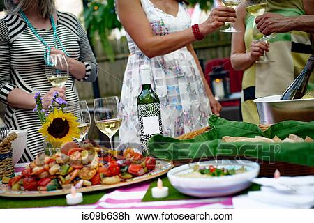 Group of people at garden party, holding wine glasses, making a toast, food on serving plates on table, mid section View Large Photo Image Stock Image - Group of people at garden party, holding wine glasses, making a toast, food on serving plates on table, mid section. Fotosearch