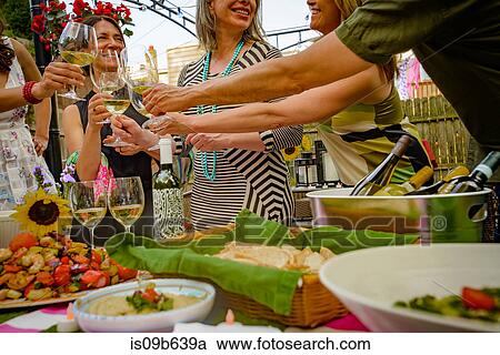 Stock Image - Group of people at garden party, holding wine glasses, making a toast, mid section. Fotosearch