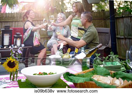 Group of people at garden party, holding wine glasses, making a toast, bottles of wine in ice bucket served food in foreground View Large Photo Image Stock Photo - Group of people at garden party, holding wine glasses, making a toast, bottles of wine in ice bucket served food in foreground. Fotosearch