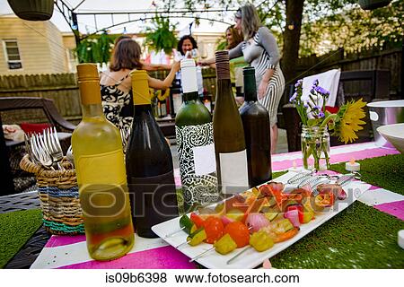 Group of people at garden party, holding wine glasses, making a toast, focus on row of wine bottles in foreground View Large Photo Image Stock Photo - Group of people at garden party, holding wine glasses, making a toast, focus on row of wine bottles in foreground. Fotosearch
