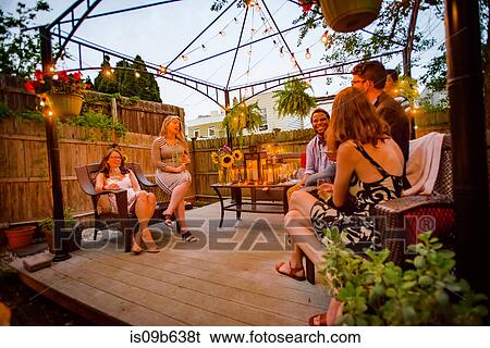Stock Photograph - Group of people at garden party, sitting on decking, in conversation. Fotosearch
